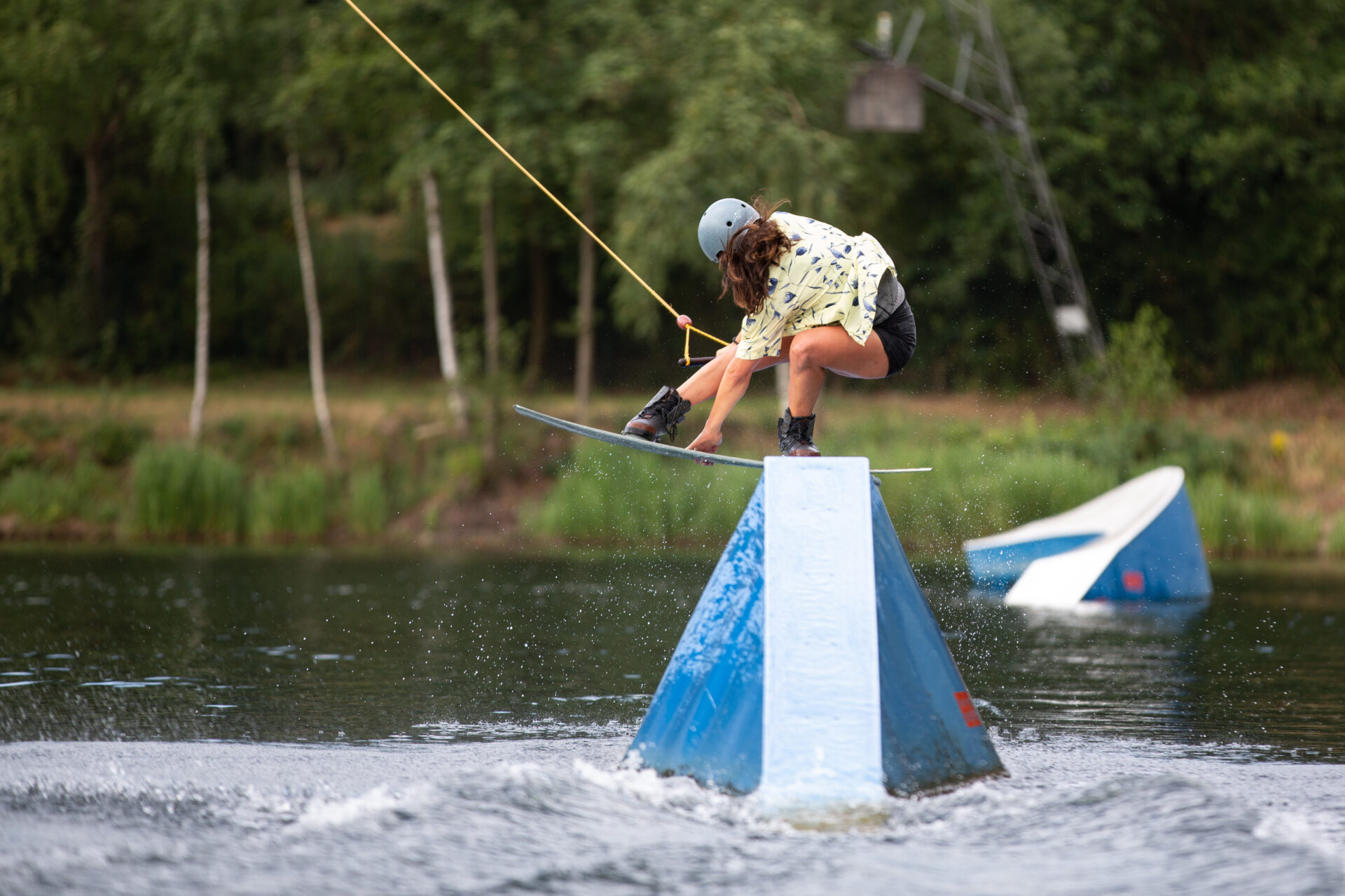 wasserski-langenfeld-girls-wake-session Pro-Wakeboarderin fährt über Funbox und berührt dabei ihr Wakeboard mittig zwischen der Bindung