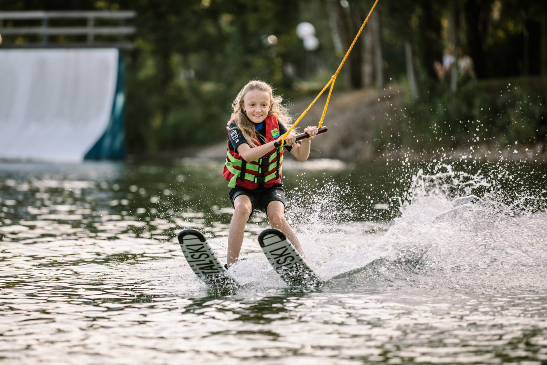 wasserski-langenfeld-minibahn-kind Mädchen fährt in Anfängerausrüstung mit Wasserskiern an der Minibahn
