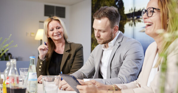 Zwei Frauen und ein Mann bei einer Konferenz im Tagungsraum. Die Frauen lachen.