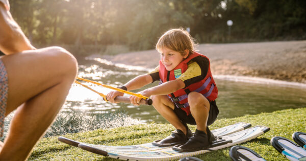 Kleiner Junge sitzt in der Hocke und macht Wasserski-Trockenübung zusammen mit einem Trainer