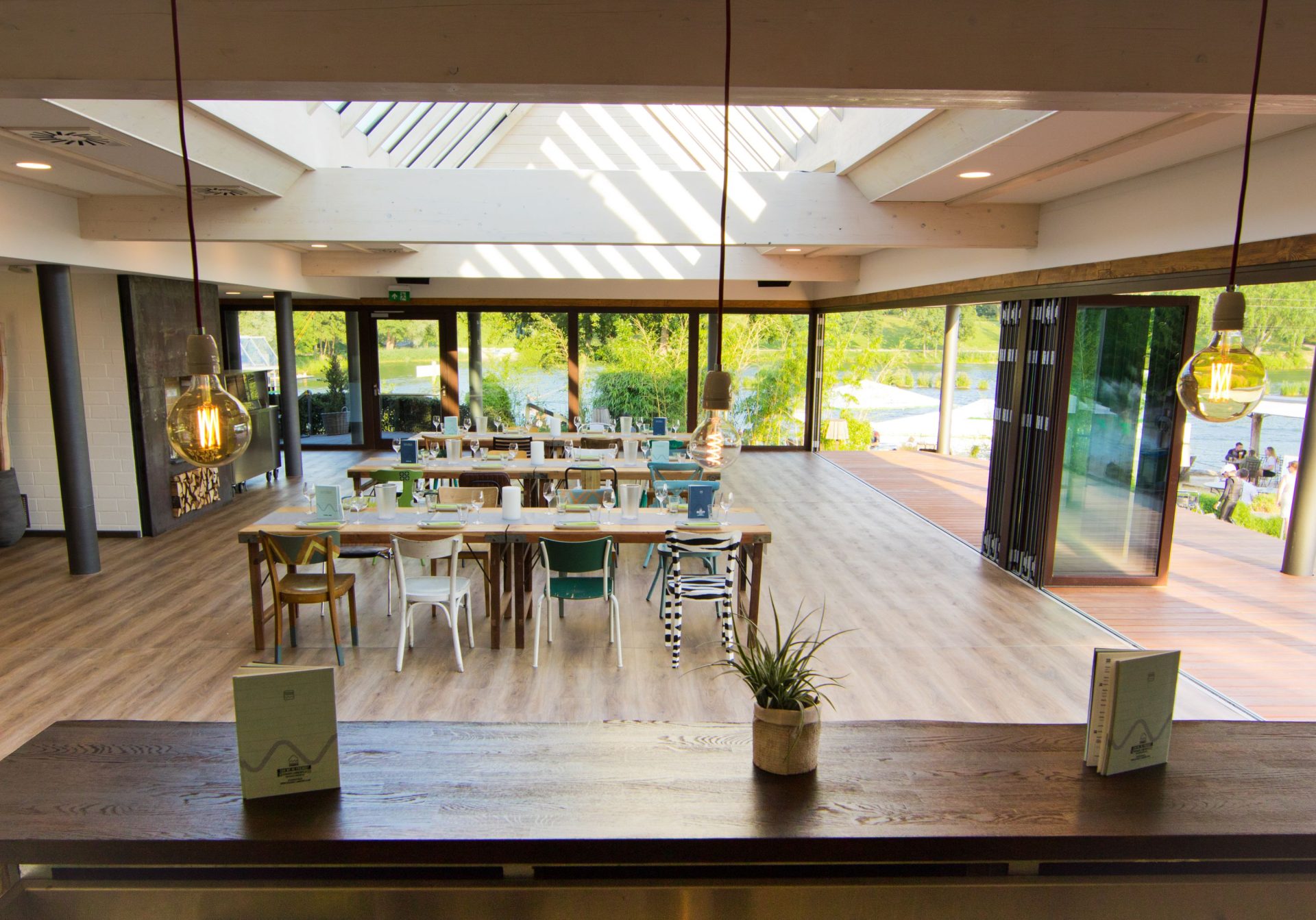 Der Eventraum aus Blick der Bar mit gedeckten Tischen und geöffneten Fensterfronten