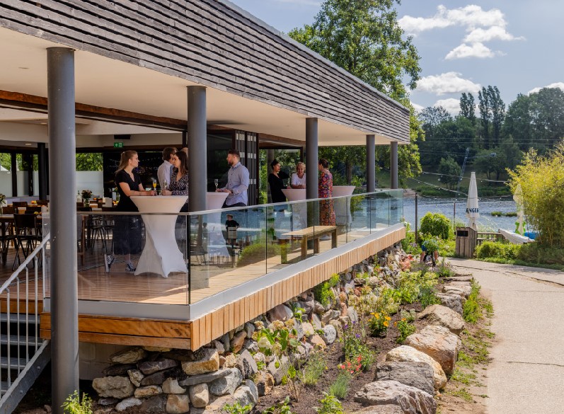 Eventraum_Seehaus_Langenfeld_Außenansicht_Terrasse_Menschen an Stehtischen_Sonne