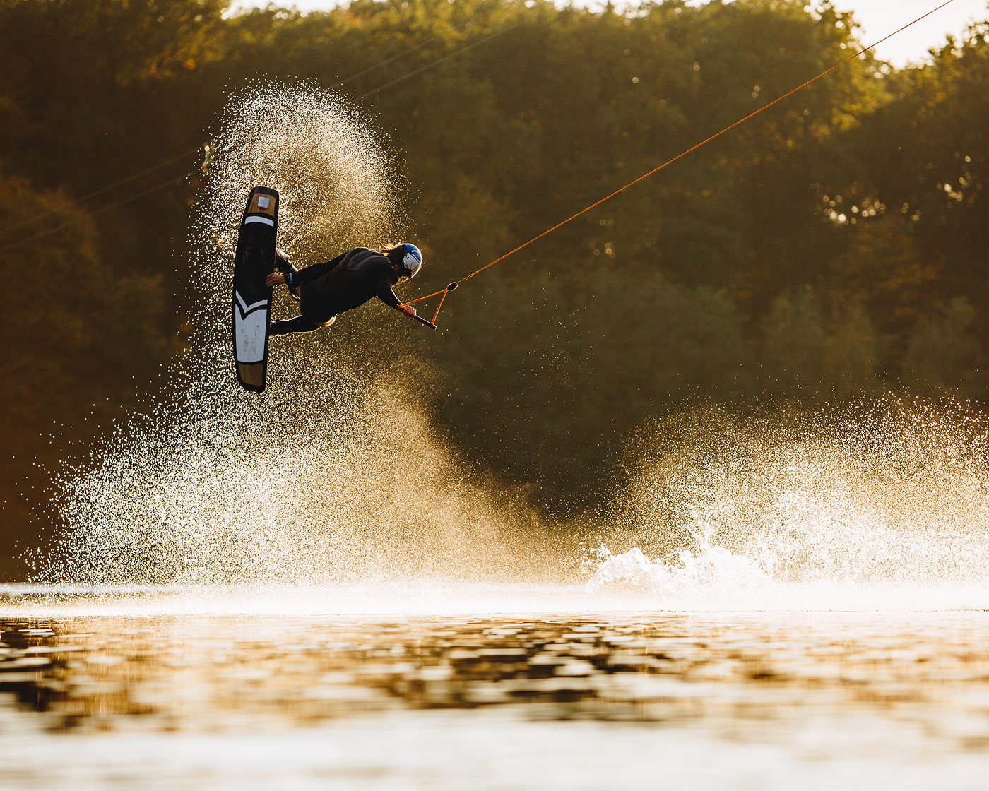 Wakeboarder springt in morgendlicher Dämmerung aus dem Wasser und grabt dabei sein Wakeboard.