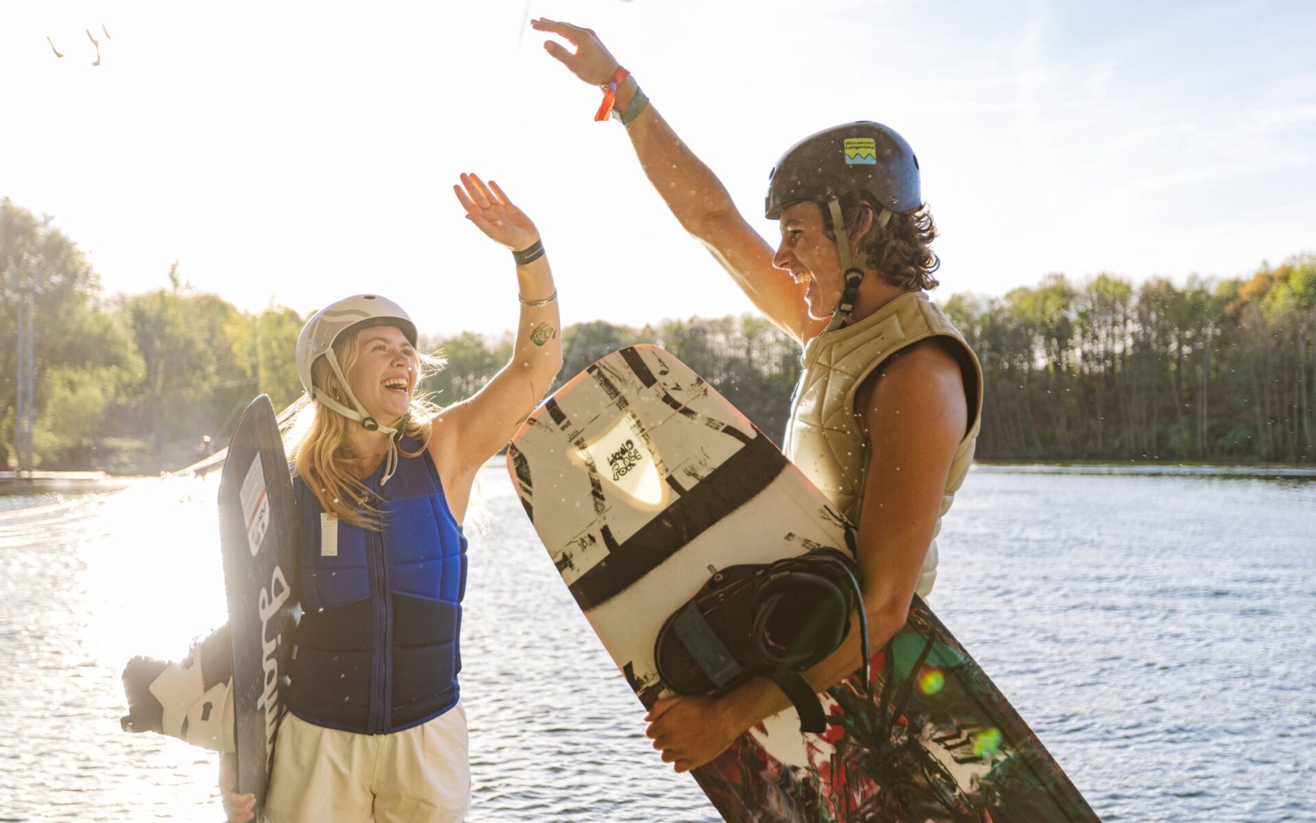 Mädchen und Junge mit Wakeboards unter dem Arm geben sich auf dem Startplatz ein High Five.