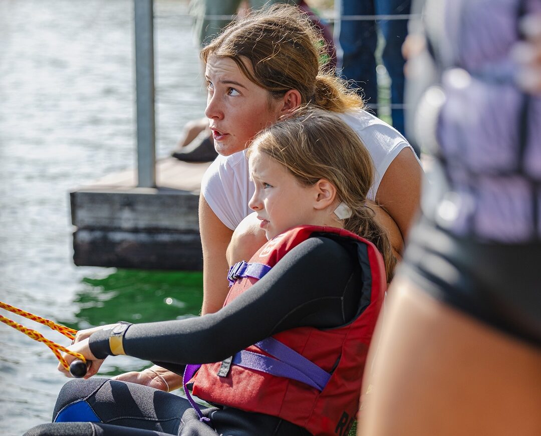 Eine Trainerin gibt einem jungen Mädchen Hilfe beim Starten auf dem Wakeboard.