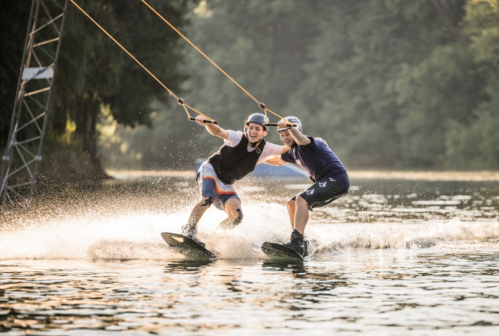 Zwei Freunde fahren zusammen nebeneinander Wakeboard und liegen sich dabei in den Armen.